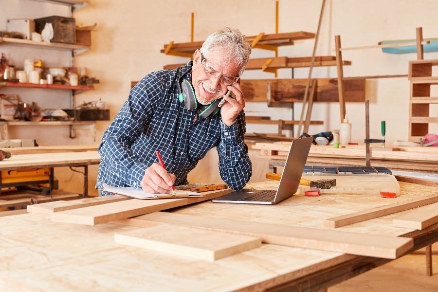 A small-business owner smiling on the phone while working in his woodworking workshop